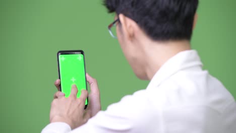 Young-Asian-businessman-using-phone-while-showing-copy-space