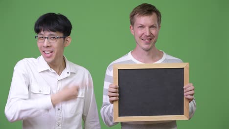 Two-happy-young-multi-ethnic-businessmen-showing-blackboard-and-giving-thumbs-up