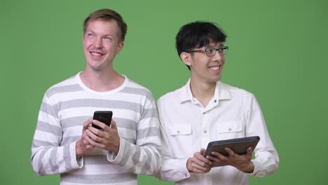 Two-happy-young-multi-ethnic-businessmen-using-phone-and-digital-tablet-for-social-media-concept