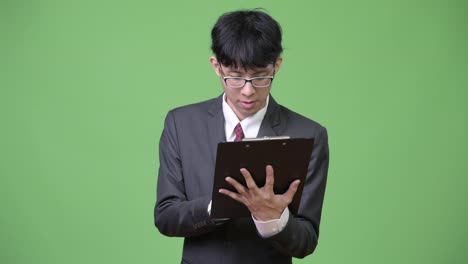 Young-Asian-businessman-reading-with-clipboard-and-talking-to-the-side