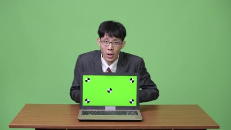 Young-happy-Asian-businessman-feeling-excited-while-talking-and-showing-laptop-to-camera