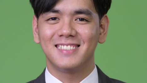 Happy-young-handsome-Asian-businessman-smiling-against-green-background