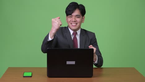 Young-handsome-Asian-businessman-working-with-laptop-against-green-background