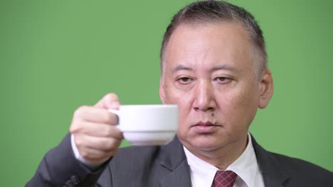 Reife-japanischer-Geschäftsmann-halten-Kaffeetasse-auf-den-Kopf-gestellt