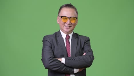 Mature-Japanese-businessman-wearing-sunglasses-against-green-background