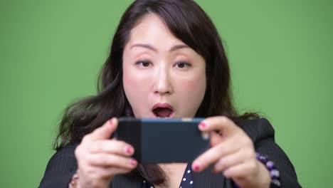 Mature-beautiful-Asian-businesswoman-using-phone-and-looking-shocked