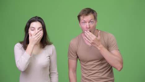 Young-couple-looking-shocked-together-against-green-background