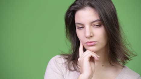 Young-beautiful-woman-thinking-while-looking-down-against-green-background