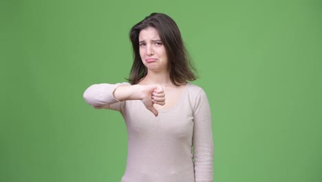 Young-sad-woman-giving-thumbs-down-against-green-background