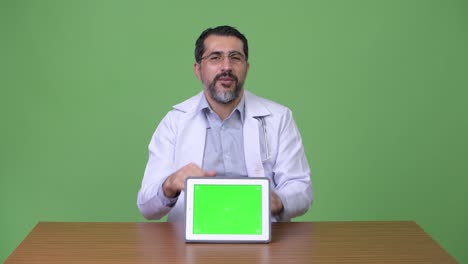 Handsome-Persian-bearded-man-doctor-giving-thumbs-up-while-showing-digital-tablet