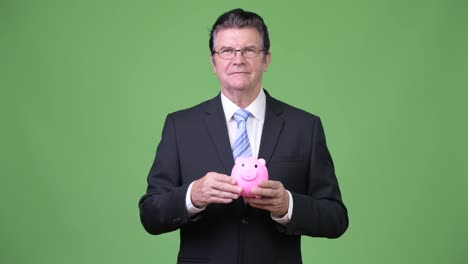 Senior-gut-aussehend-Geschäftsmann-hält-Sparschwein-und-Daumen-aufgeben