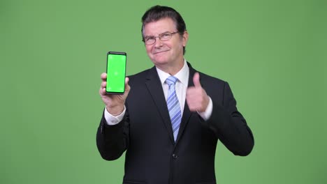 Senior-handsome-businessman-showing-phone-and-giving-thumbs-up