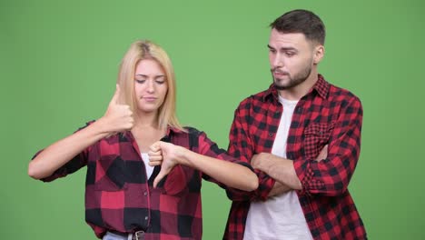 Young-woman-being-indecisive-with-young-man-waiting-with-arms-crossed