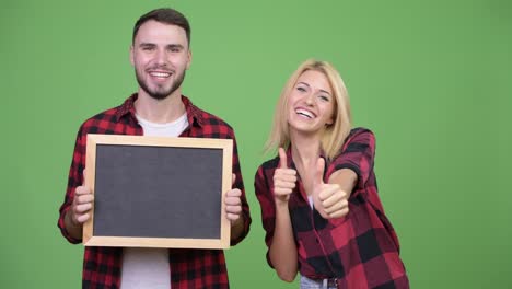 Young-couple-holding-blackboard-and-giving-thumbs-up-together