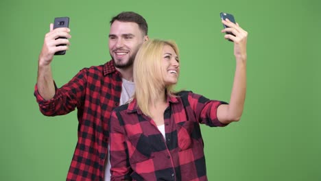 Young-couple-using-phone-and-taking-selfies-together