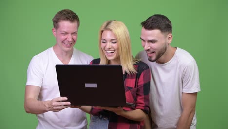 Three-happy-young-friends-smiling-while-using-laptop-together