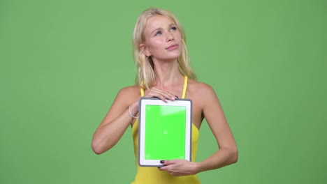 Young-happy-beautiful-blonde-woman-thinking-while-showing-digital-tablet