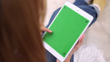 Young-asian-woman-using-black-tablet-device-with-green-screen.-Asian-woman-holding-tablet,-scrolling-pages-while-sitting-on-the-couch-in-the-living-room.-Chroma-key.