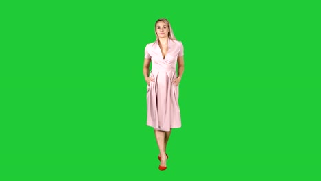 Woman-in-pink-dress-with-hands-in-pockets-is-walking-towards-the-camera-on-a-Green-Screen,-Chroma-Key