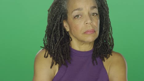 Older-African-American-woman-with-dreadlocks-looks-upset-and-then-laughs,-on-a-green-screen-studio-background