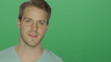 Young-man-smiles-charmingly,-on-a-green-screen-studio-background
