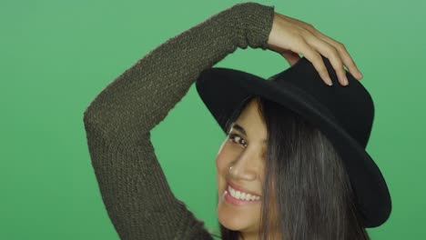 Young-woman-wearing-a-hat-and-being-playful-and-posing,-on-a-green-screen-studio-background