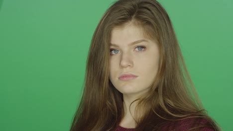 Young-brunette-woman-runs-her-fingers-through-her-hair-stares-blankly,-on-a-green-screen-studio-background