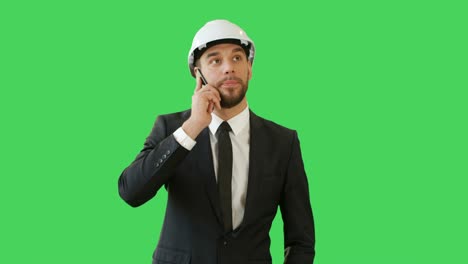 Medium-Shot-of-a-Businessman-in-a-Hard-Hat-Talking-on-the-Phone-and-Waving-Hello-to-Somebody.-Background-is-Green-Screen.