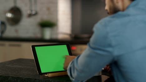 In-the-Kitchen.-Young-Man-Sips-From-a-Cup-While-Using--Tablet-Computer-with-Green-Screen.