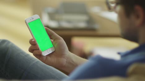 Man-is-Holding-Phone-with-Green-Screen-in-Portrait-Mode-at-Home