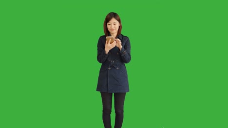 Junge-asiatische-Frau-trägt-einen-blauen-Mantel.-Verwendung-von-Smartphone,-Digital-Tablette-und-Blick-in-die-Kamera.-Frau-stand-vor-einem-Greenscreen-für-Chroma-Key.