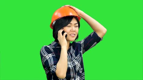 Female-engineer-with-orange-helmet-having-a-phone-call-via-smartphone-on-a-Green-Screen,-Chroma-Key