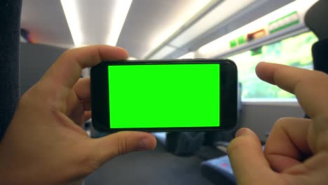 Hands-Holding-a-Phone-with-a-Green-Screen-on-the-Train