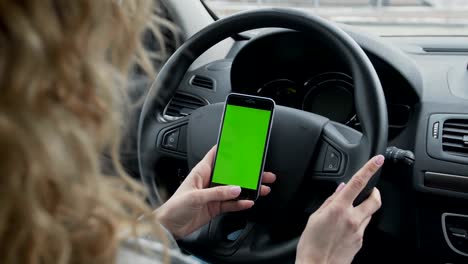 Woman-sits-in-the-modern-car-and-works-on-smartphone---closeup-hands.-Green-screen.Chroma-key