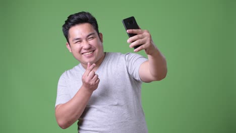 Young-handsome-overweight-Asian-man-against-green-background