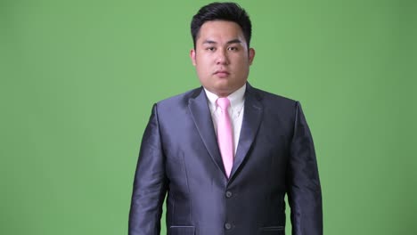 Young-handsome-overweight-Asian-businessman-against-green-background