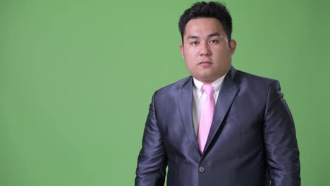 Young-handsome-overweight-Asian-businessman-against-green-background