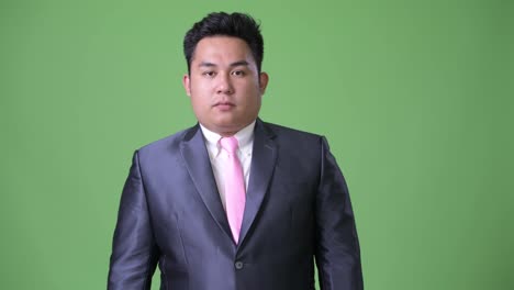 Young-handsome-overweight-Asian-businessman-against-green-background