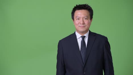 Mature-Japanese-businessman-against-green-background