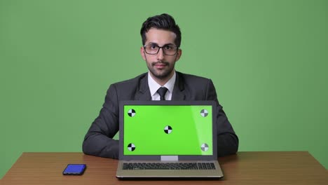 Young-handsome-bearded-Persian-businessman-against-green-background