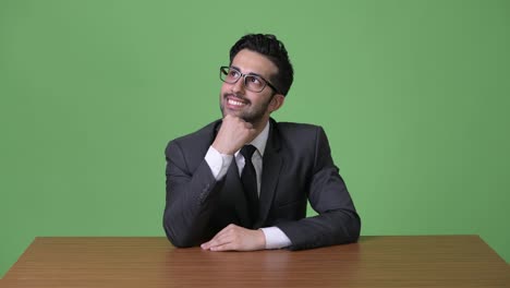 Young-handsome-bearded-Persian-businessman-against-green-background