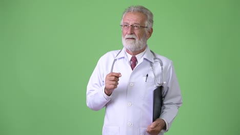 Handsome-senior-bearded-man-doctor-against-green-background