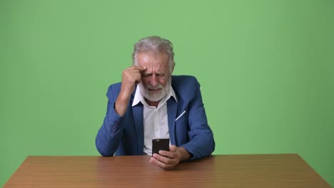 Handsome-senior-bearded-businessman-against-green-background