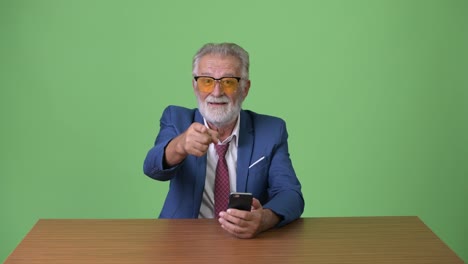 Handsome-senior-bearded-businessman-against-green-background