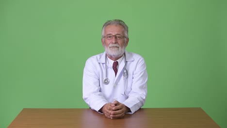 Handsome-senior-bearded-man-doctor-against-green-background