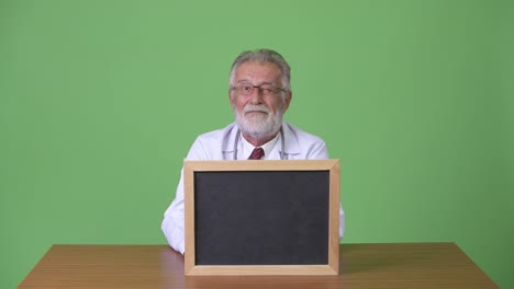 Handsome-senior-bearded-man-doctor-against-green-background