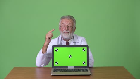 Handsome-senior-bearded-man-doctor-against-green-background