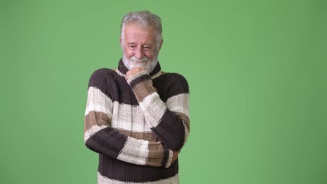 Handsome-senior-bearded-man-wearing-warm-clothing-against-green-background