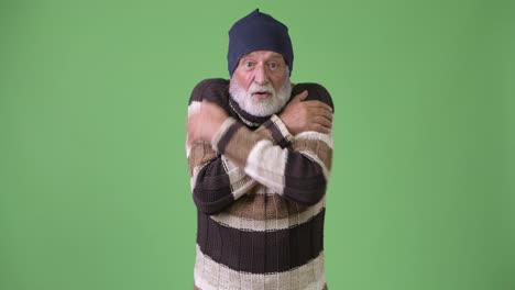 Handsome-senior-bearded-man-wearing-warm-clothing-against-green-background