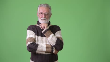 Handsome-senior-bearded-man-wearing-warm-clothing-against-green-background